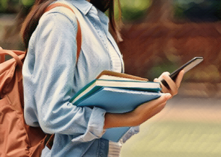 teenage girl holding phone and books wearing backpack at school